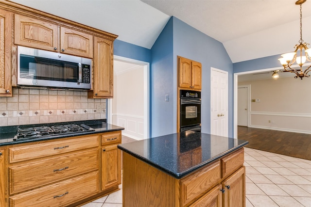 kitchen with light tile patterned floors, appliances with stainless steel finishes, a kitchen island, decorative light fixtures, and vaulted ceiling