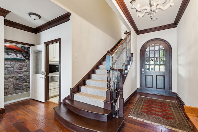 foyer entrance featuring crown molding, dark wood-type flooring, and an inviting chandelier