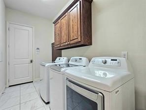 clothes washing area featuring separate washer and dryer, light tile patterned floors, and cabinets