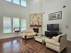 living room featuring a towering ceiling, dark hardwood / wood-style flooring, and a stone fireplace