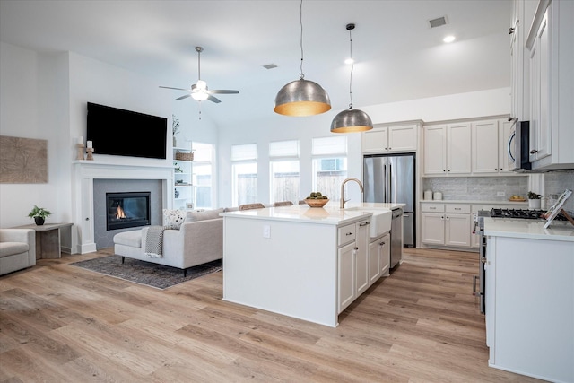 kitchen with hanging light fixtures, stainless steel appliances, light hardwood / wood-style floors, an island with sink, and white cabinets