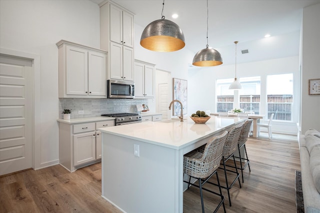 kitchen with a breakfast bar area, tasteful backsplash, hanging light fixtures, appliances with stainless steel finishes, and a kitchen island with sink