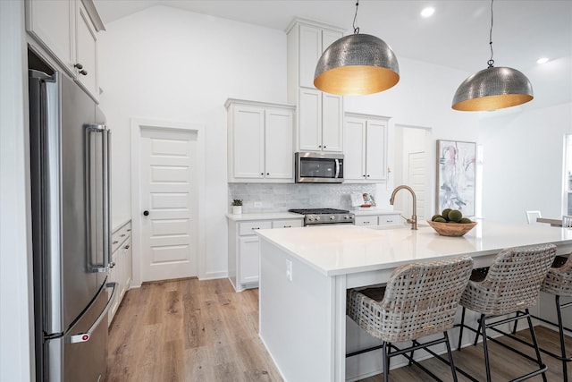 kitchen featuring sink, a center island with sink, high quality appliances, pendant lighting, and white cabinets