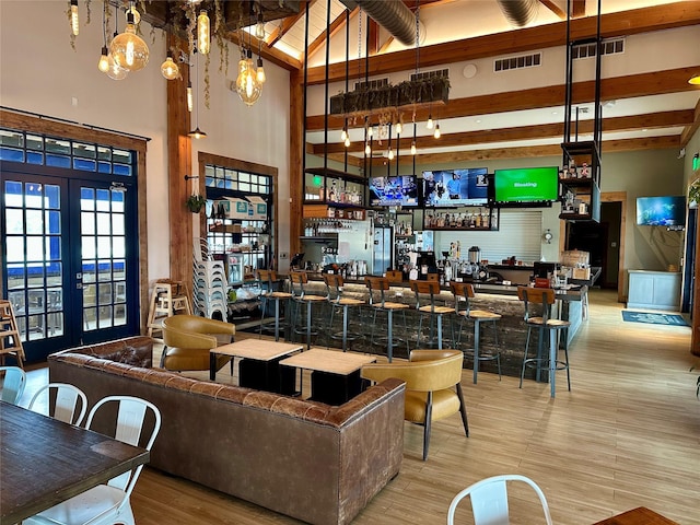 bar with a towering ceiling, pendant lighting, beamed ceiling, light hardwood / wood-style floors, and french doors