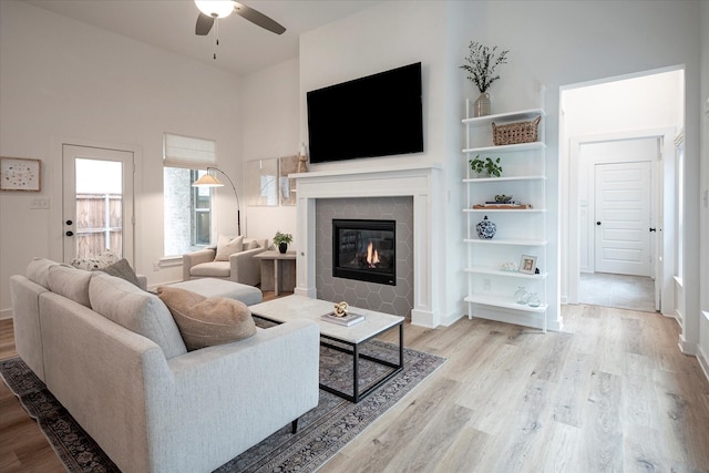 living room featuring a tiled fireplace, a towering ceiling, ceiling fan, and light wood-type flooring