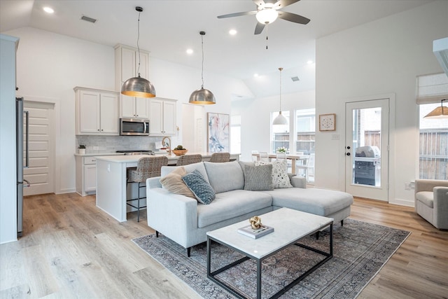 living room with ceiling fan, high vaulted ceiling, and light wood-type flooring