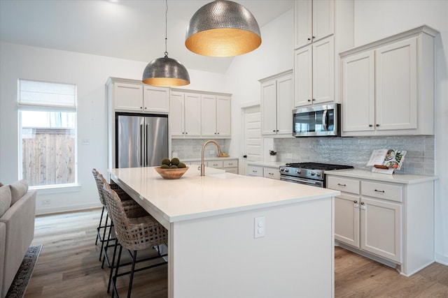 kitchen with sink, stainless steel appliances, a kitchen breakfast bar, a center island with sink, and decorative light fixtures