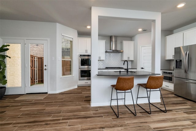 kitchen featuring white cabinets, wall chimney exhaust hood, stainless steel appliances, and wood finish floors