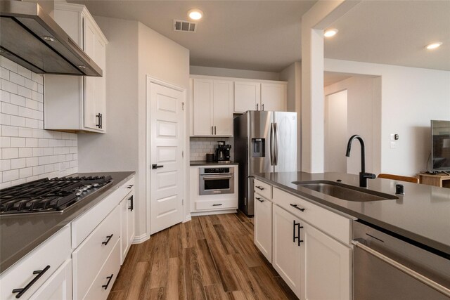 kitchen featuring dark wood-type flooring, wall chimney exhaust hood, sink, white cabinetry, and appliances with stainless steel finishes