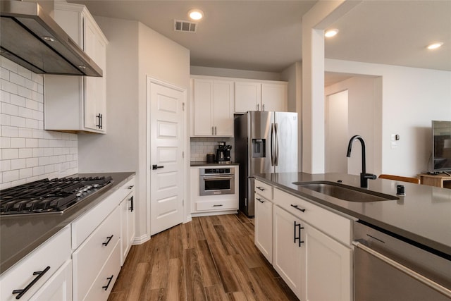 kitchen with stainless steel appliances, dark countertops, visible vents, a sink, and wall chimney exhaust hood