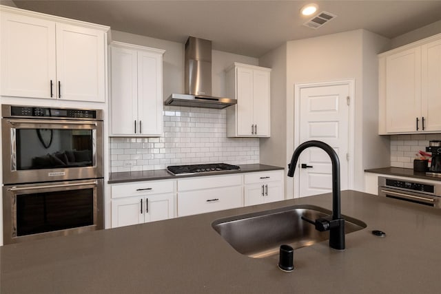 kitchen with sink, white cabinetry, tasteful backsplash, stainless steel appliances, and wall chimney range hood