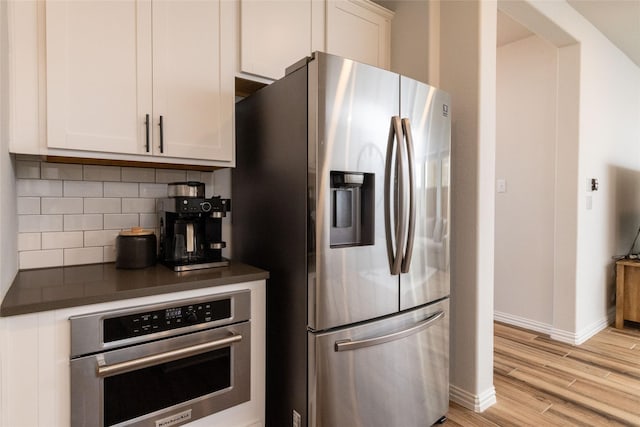 kitchen featuring stainless steel appliances, dark countertops, decorative backsplash, light wood-style floors, and white cabinets