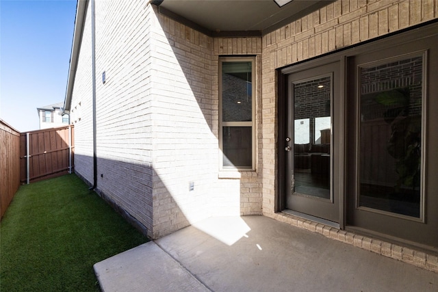 doorway to property with fence, a lawn, and brick siding