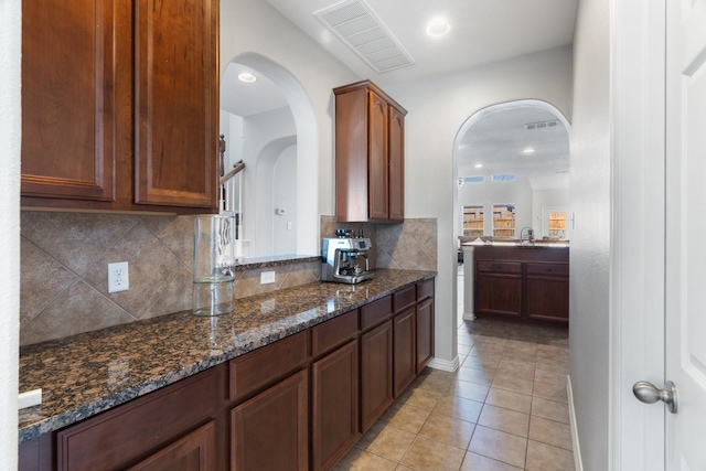 kitchen with dark stone countertops, light tile patterned floors, backsplash, and sink