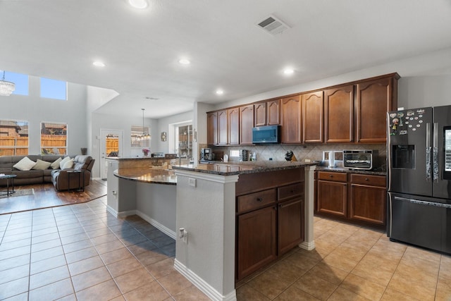 kitchen with refrigerator with ice dispenser, light tile patterned floors, dark stone countertops, a kitchen island, and decorative light fixtures