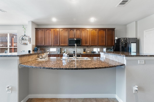 kitchen with sink, backsplash, kitchen peninsula, black refrigerator with ice dispenser, and dark stone counters