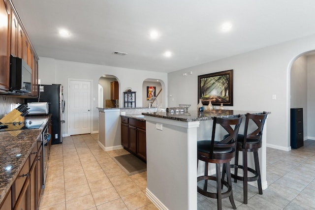 kitchen featuring sink, a breakfast bar, dark stone counters, and a center island with sink