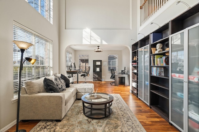 living room featuring wood-type flooring, a healthy amount of sunlight, and a towering ceiling