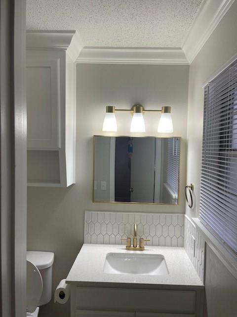 bathroom with tasteful backsplash, ornamental molding, toilet, and vanity