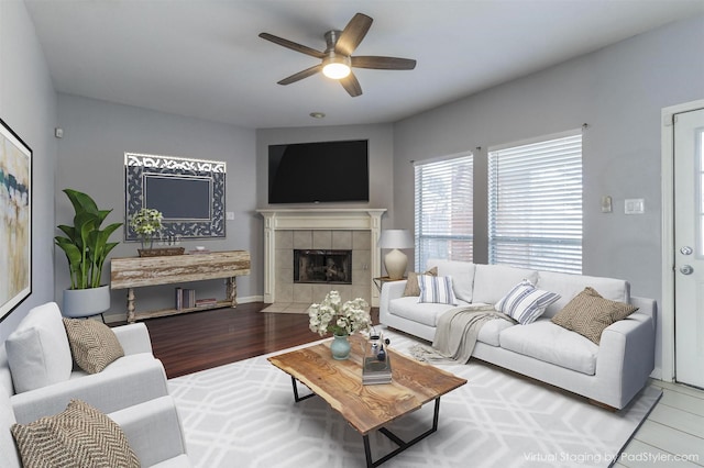 living room with a tiled fireplace, ceiling fan, and light hardwood / wood-style flooring