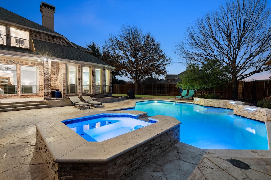 pool at dusk featuring an in ground hot tub and a patio