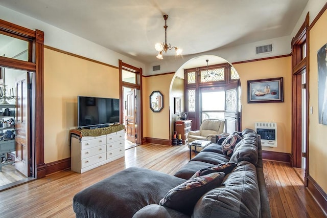 living room with heating unit, an inviting chandelier, and light hardwood / wood-style flooring