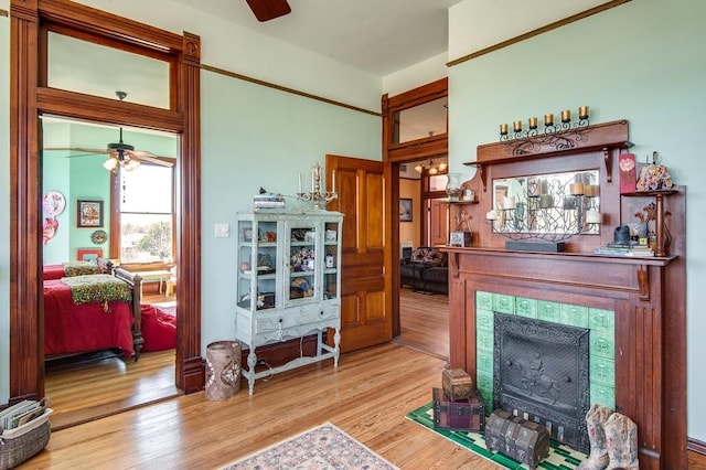 living room featuring ceiling fan, a tile fireplace, and light wood-type flooring