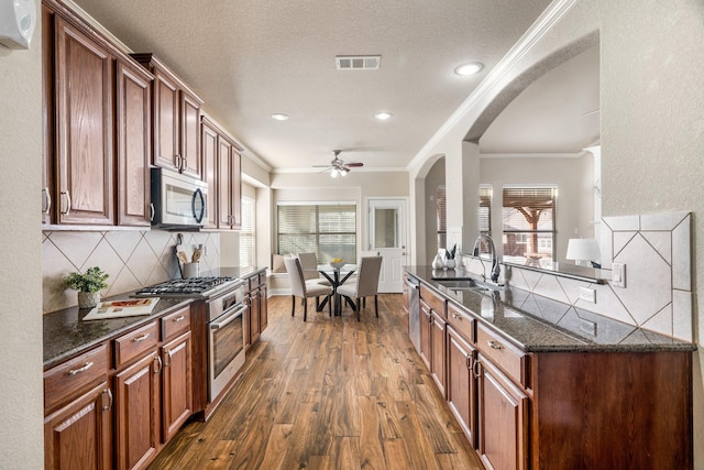 kitchen with sink, ornamental molding, appliances with stainless steel finishes, dark hardwood / wood-style flooring, and dark stone counters