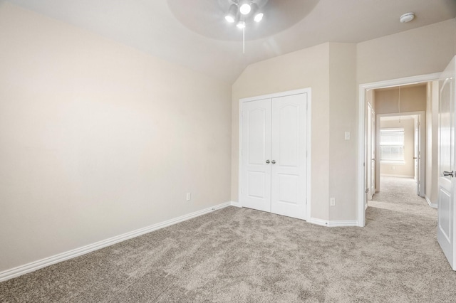 unfurnished bedroom featuring light carpet, vaulted ceiling, a closet, and ceiling fan