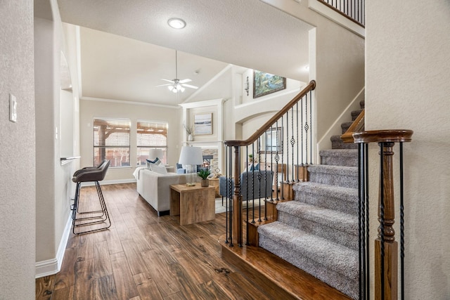 stairway featuring ornamental molding, wood-type flooring, high vaulted ceiling, and ceiling fan