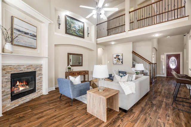 living room featuring dark wood-type flooring, a towering ceiling, and a stone fireplace