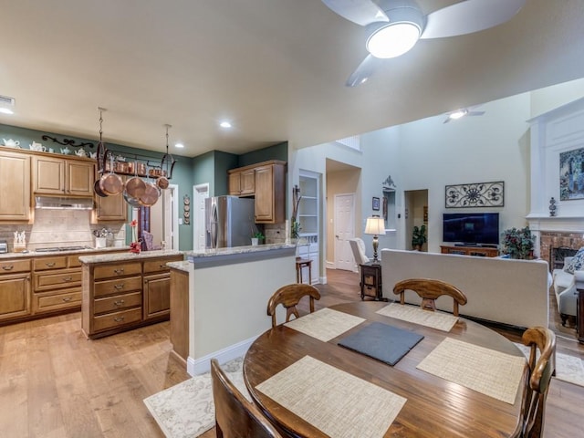 dining area featuring a fireplace, ceiling fan, and light wood-type flooring