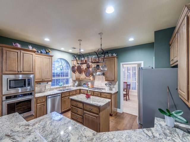 kitchen with light stone countertops, decorative backsplash, appliances with stainless steel finishes, a sink, and wood finished floors