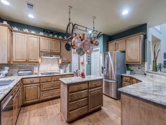 kitchen featuring light stone countertops, under cabinet range hood, light wood-type flooring, and appliances with stainless steel finishes