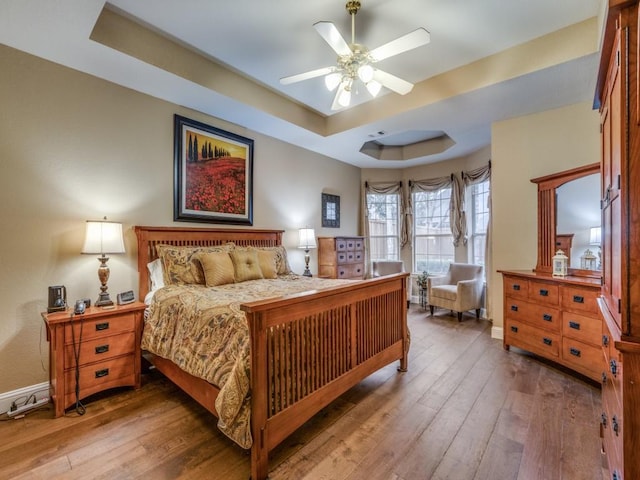 bedroom with hardwood / wood-style flooring, baseboards, and a tray ceiling