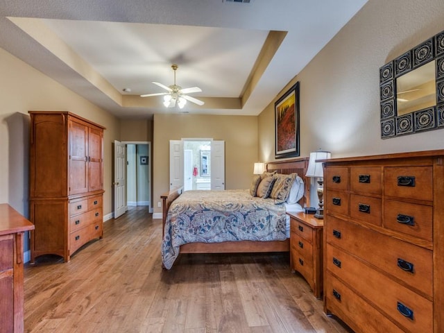 bedroom featuring baseboards, visible vents, a ceiling fan, a tray ceiling, and light wood-style floors