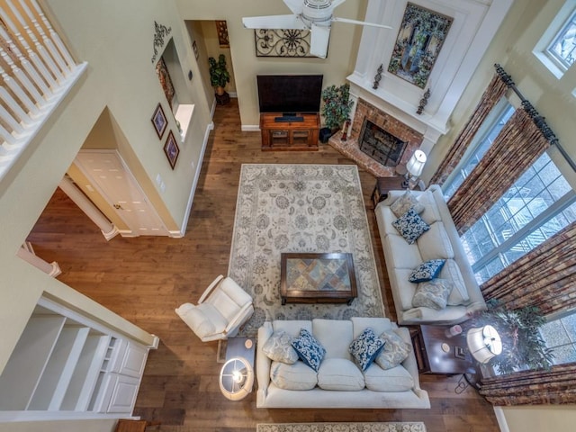 living room with hardwood / wood-style flooring, ceiling fan, a brick fireplace, and a high ceiling