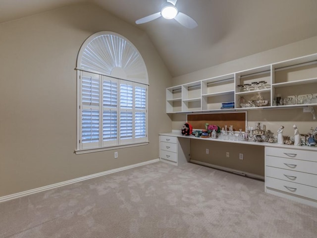 unfurnished office with built in desk, light colored carpet, a ceiling fan, vaulted ceiling, and baseboards