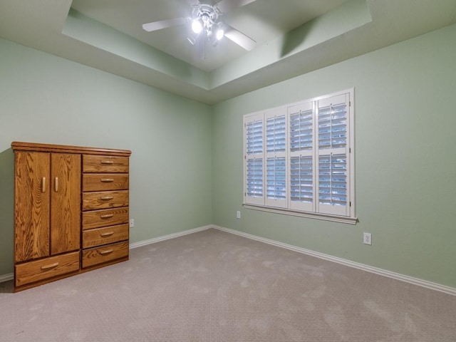 unfurnished bedroom featuring ceiling fan, carpet, a raised ceiling, and baseboards