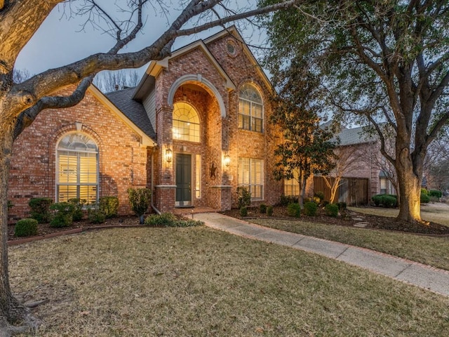 traditional-style home with roof with shingles, a front yard, fence, and brick siding