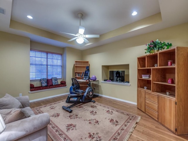 interior space featuring ceiling fan, light wood-style flooring, visible vents, baseboards, and a tray ceiling