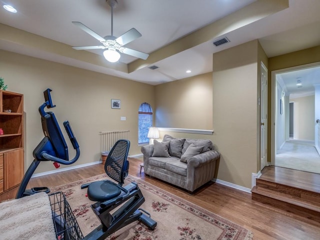 workout room featuring ceiling fan, wood-type flooring, a raised ceiling, and radiator heating unit