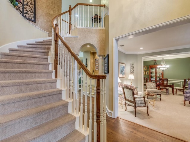 stairs with an inviting chandelier, a towering ceiling, ornamental molding, and hardwood / wood-style floors