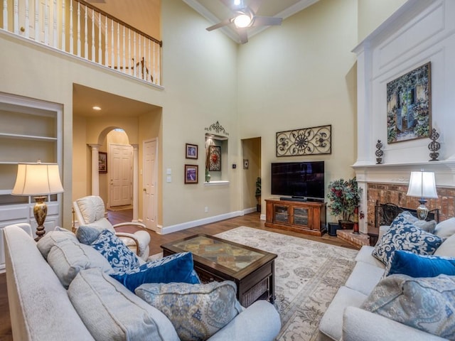 living room featuring a high ceiling, a brick fireplace, ceiling fan, and light hardwood / wood-style flooring