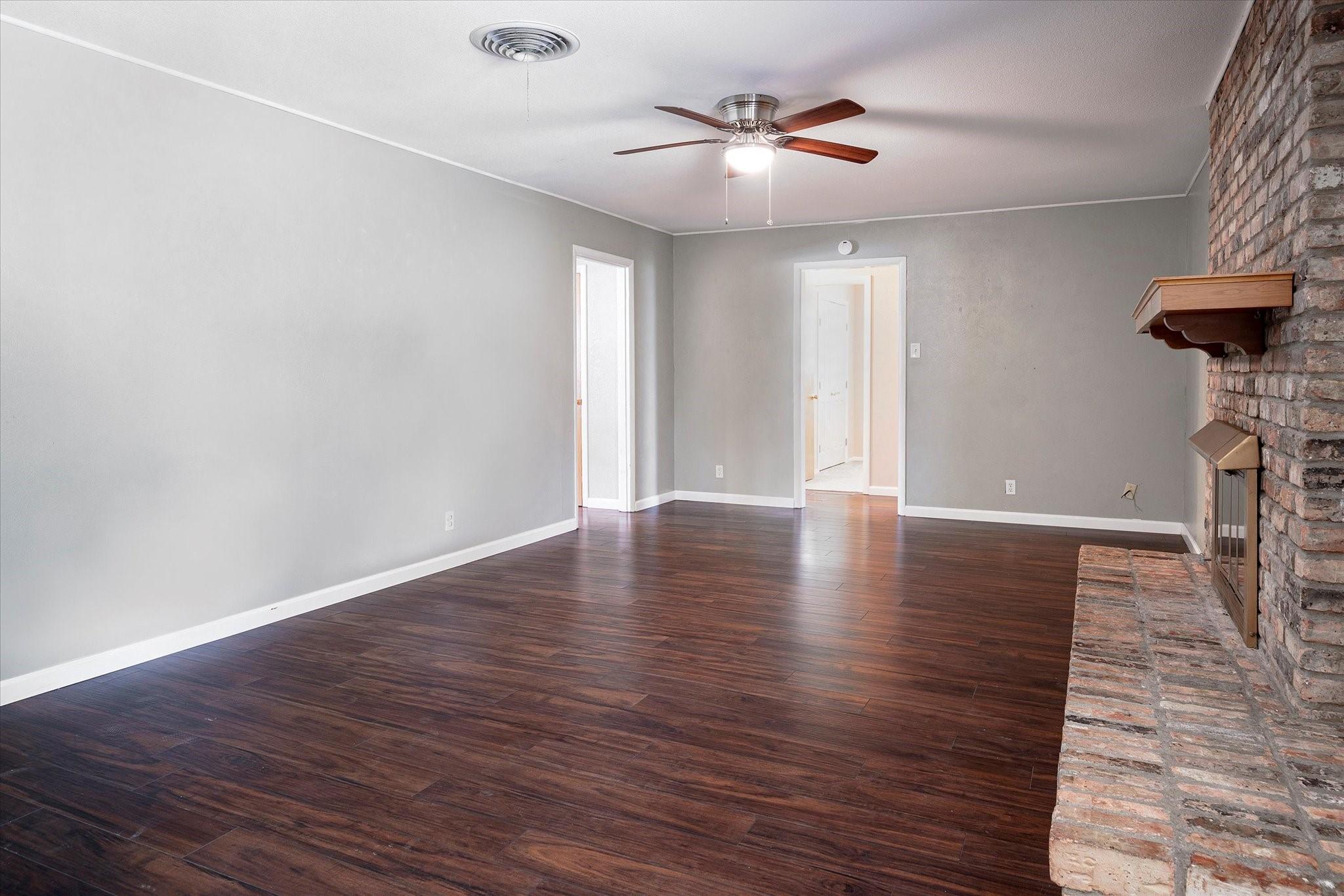 unfurnished living room with ceiling fan, a brick fireplace, and dark hardwood / wood-style flooring