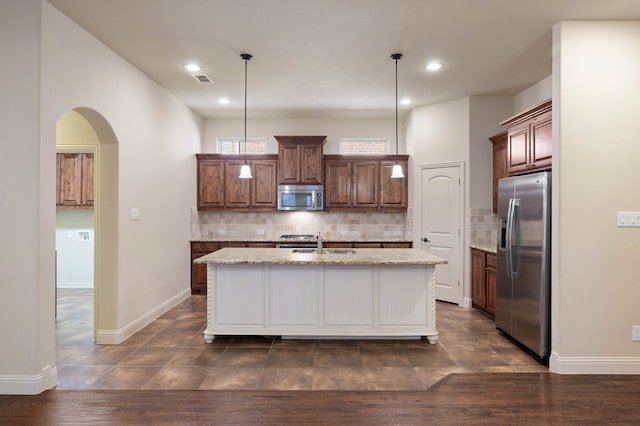 kitchen with light stone counters, tasteful backsplash, hanging light fixtures, a center island with sink, and stainless steel appliances