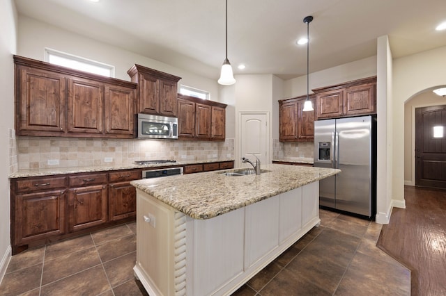 kitchen with sink, light stone counters, hanging light fixtures, an island with sink, and stainless steel appliances