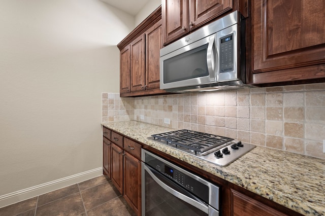 kitchen with tasteful backsplash, light stone countertops, stainless steel appliances, and dark tile patterned flooring