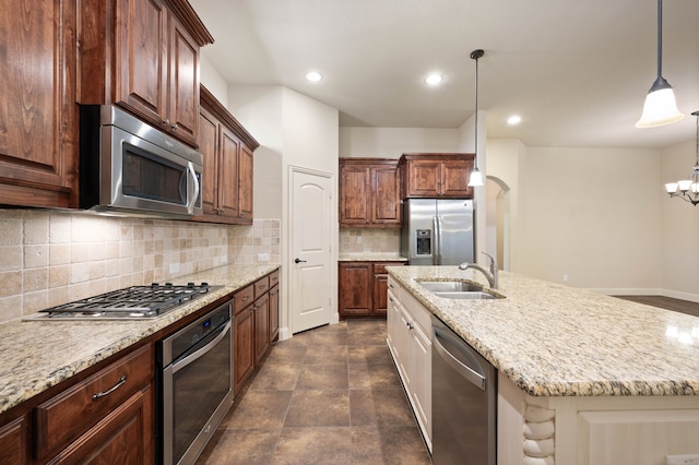 kitchen featuring appliances with stainless steel finishes, sink, decorative backsplash, hanging light fixtures, and a center island with sink