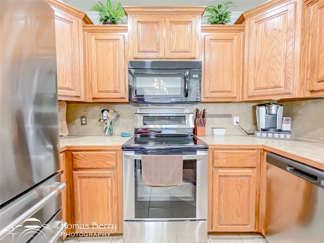 kitchen with appliances with stainless steel finishes, light tile patterned floors, backsplash, and light brown cabinetry